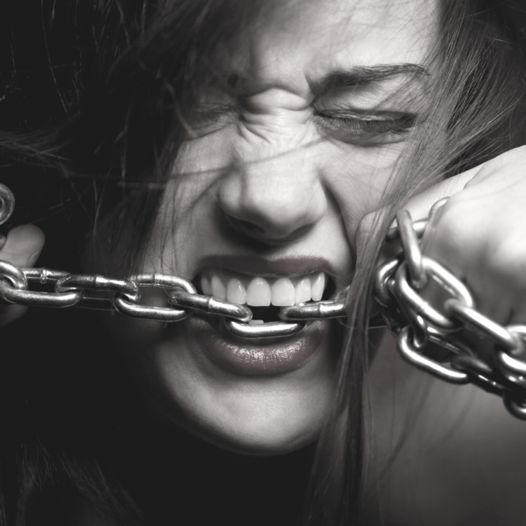 Femme mordant une chaîne en métal, symbolisant l'autosabotage et les croyances limitantes qui freinent la réussite professionnelle des femmes