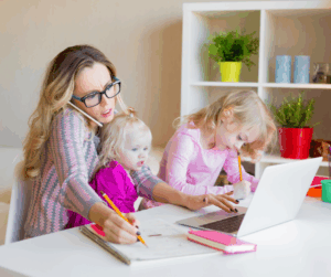 Mère au téléphone et sur ordinateur avec une petite fille sur les genoux et une autre qui dessine à côté