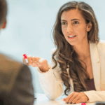 Femme souriante en discussion avec un homme, stylo à la main, illustrant une négociation salariale